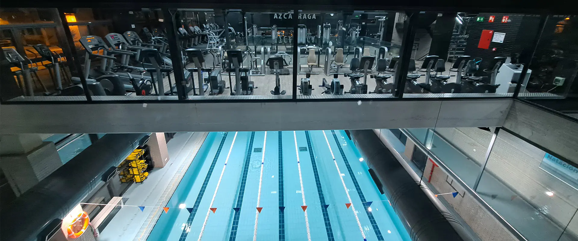 Vista frontal de la sala de fitness, con diversas máquinas de ejercicio. Vista parcial de la piscina del piso inferior