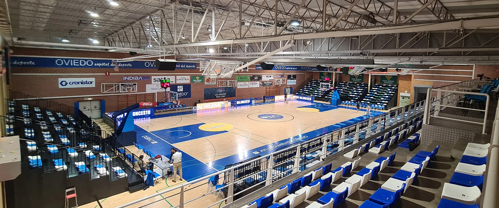Pista polideportiva desde arriba de una de las gradas. Árbitros alrededor de mesa antes del partido de baloncesto