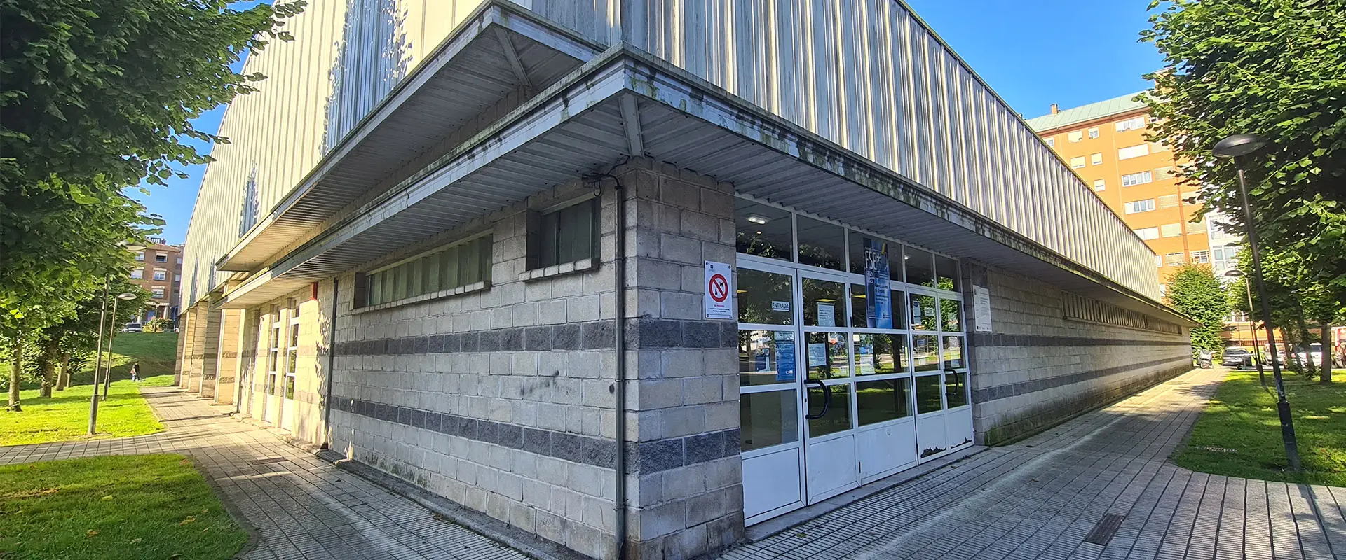 Detalle ángulo de la fachada del edificio con doble alero de hormigón y puerta metalizada blanca con rectángulos de cristal