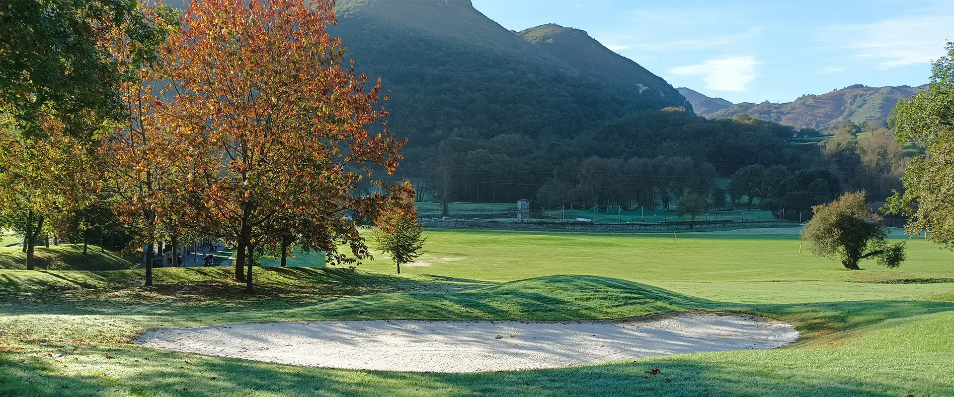 Búnker de arena, árboles alrededor y montañas al fondo