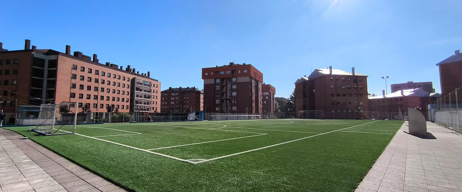 Terreno de juego a pie de campo y desde un córner, con vistas de una portería y edificios al fondo