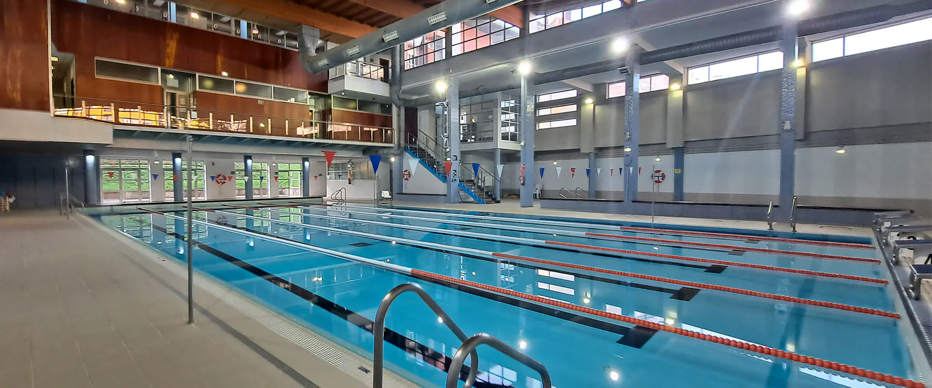 Vista lateral de la piscina principal. Barandillas de acceso en primer plano. Piso superior al fondo