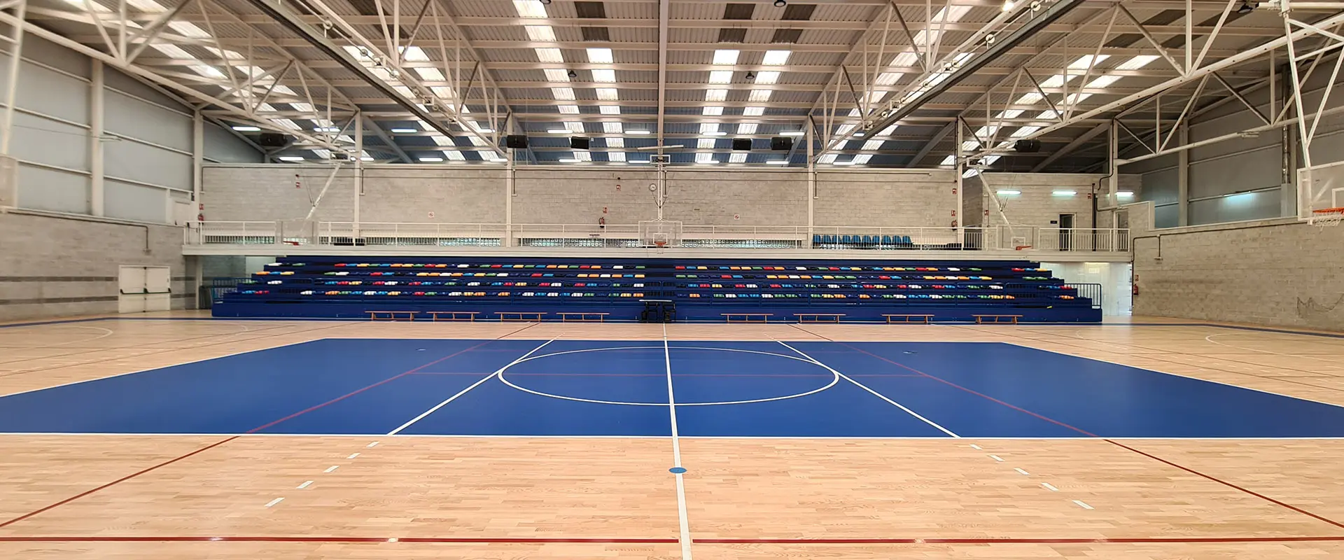 Pista polideportiva desde la cancha. Al fondo hay una grada con asientos de varios colores. A la derecha hay una canasta