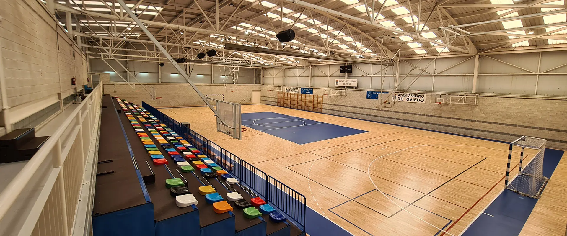Pista polideportiva desde la última fila de la grada y en ángulo. Hay porterías a izquierda y derecha y canastas en el frente