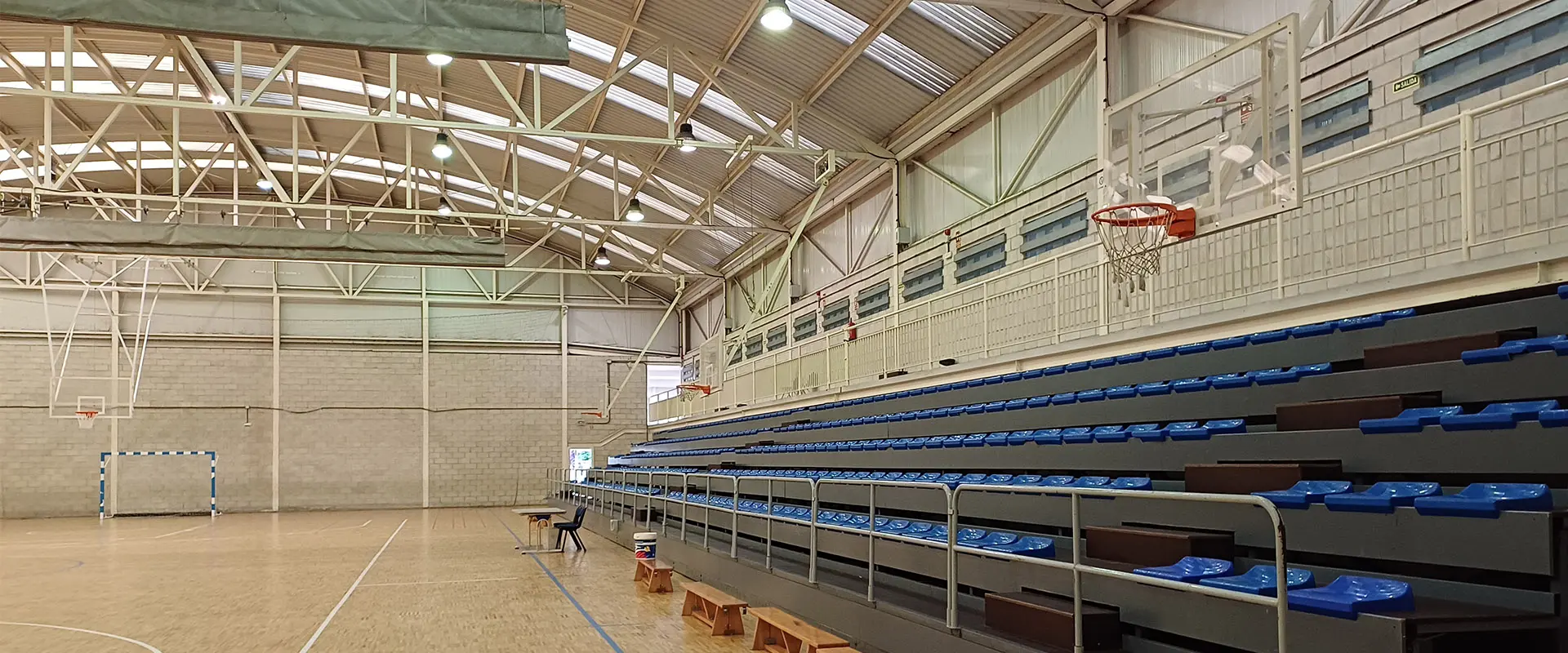 Gradas extensibles, asientos azules, desde la pista, canasta de baloncesto, bancos de madera y mesa con silla en un lateral