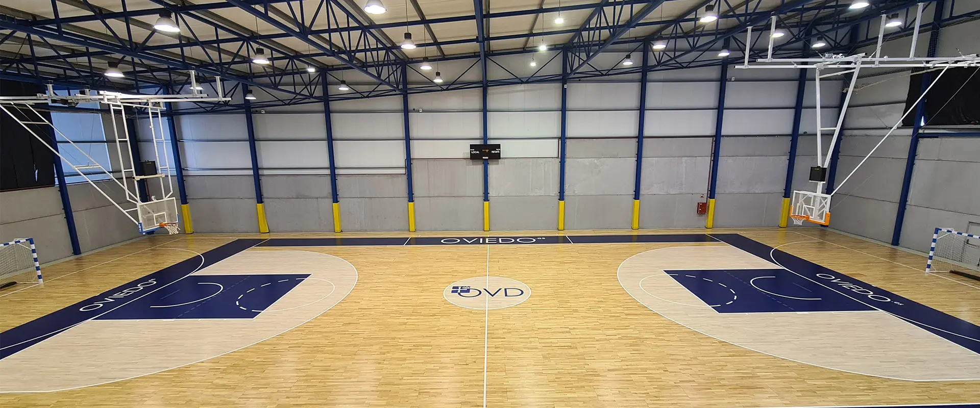 Pista polideportiva en vista lateral desde las gradas, con canastas de baloncesto y porterías de fútbol