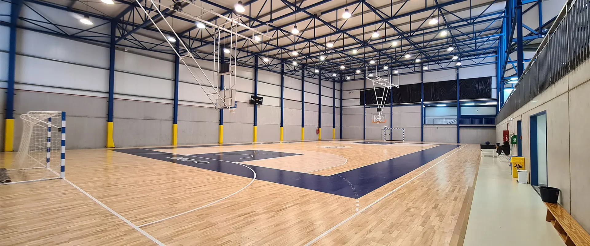 Pista polideportiva a pie de cancha, con portería en primer plano y bancos y barandilla de gradas a un lado