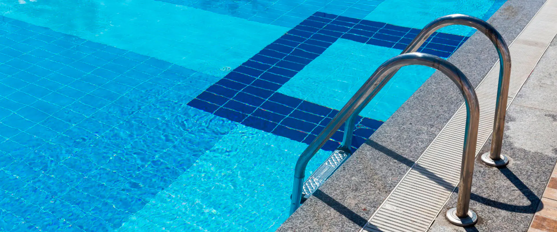 Vista parcial de una piscina con agua, con detalle de las barandillas de acceso y los azulejos del fondo