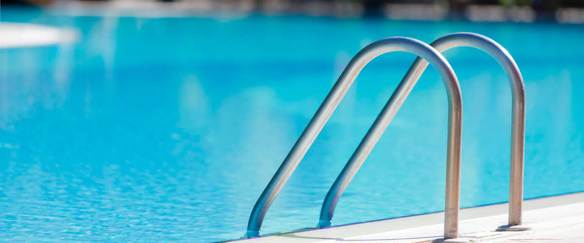 Vista parcial de una piscina con agua, con detalle de las barandillas de acceso