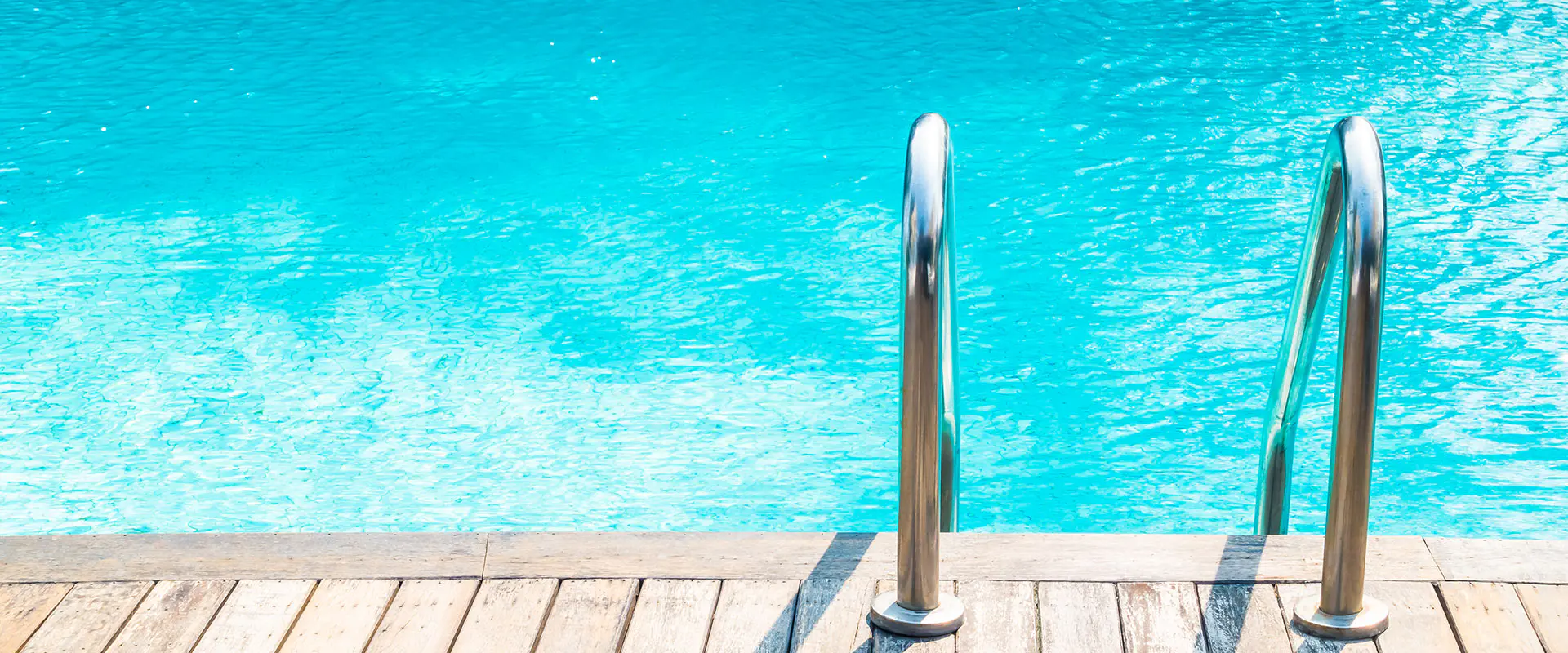 Vista parcial de una piscina con agua, con detalle del suelo de tarima y las barandillas de acceso
