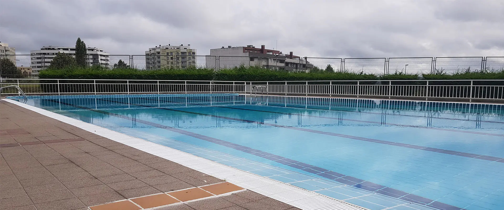 Vista parcial de la piscina principal, con las vallas perimetrales y edificios circundantes al fondo