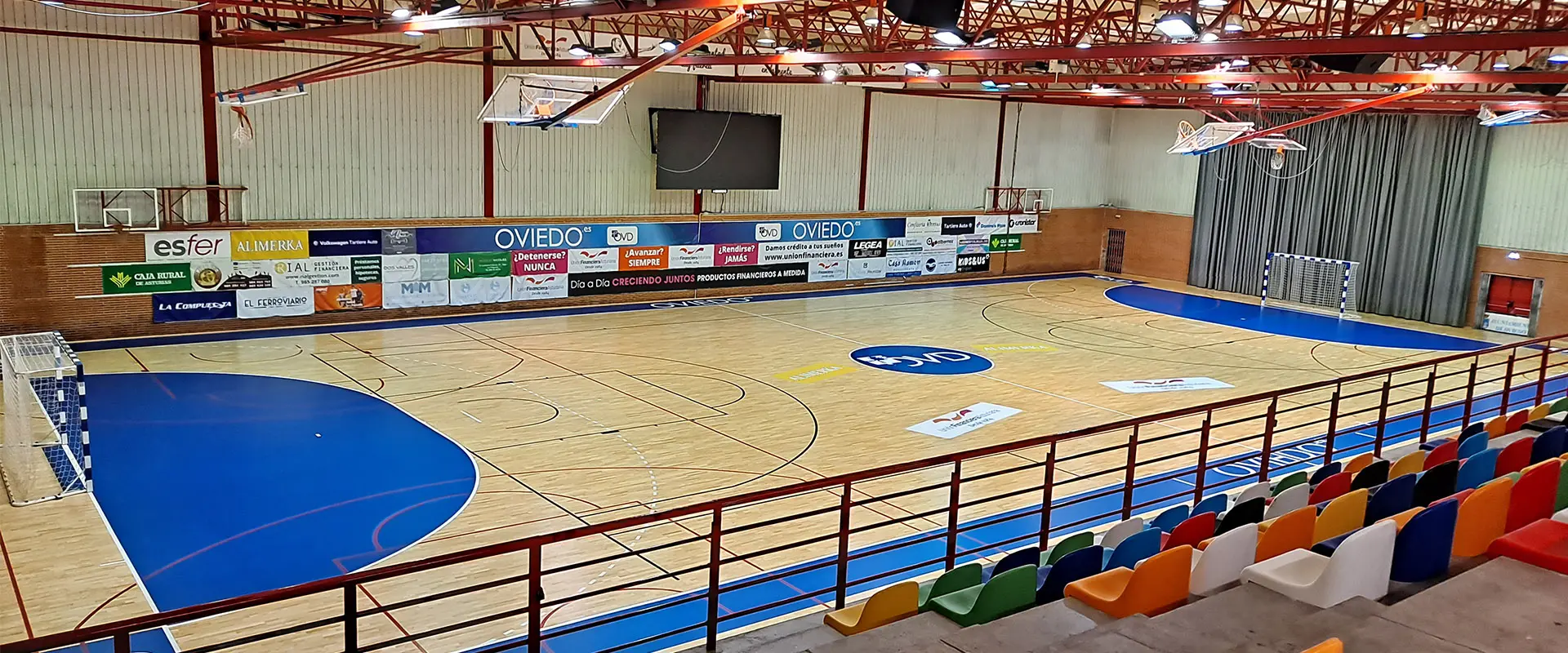 Pista polideportiva desde la parte de arriba de la grada con asientos verdes, naranjas, azules, rojos entre otros