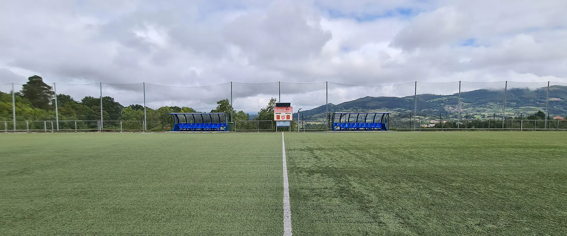 Vista frontal a pie de campo del terreno de juego, con la línea central y los banquillos y un marcador al fondo