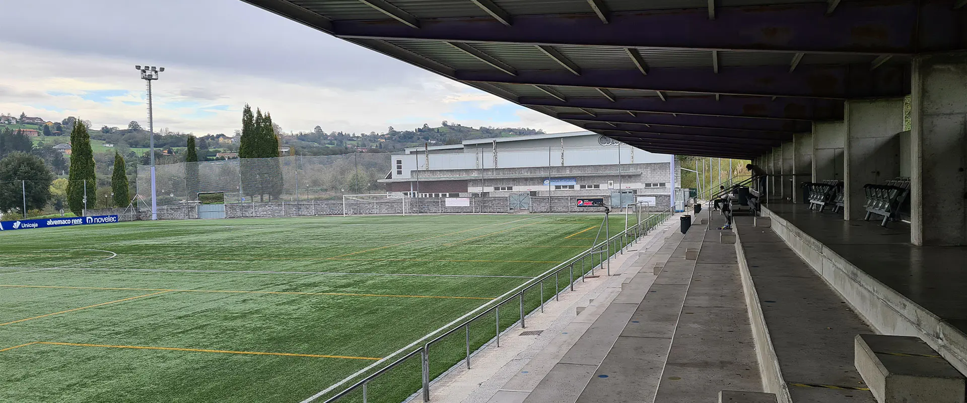 Vista lateral de las gradas de cemento cubiertas, con el terreno de juego a la izquierda