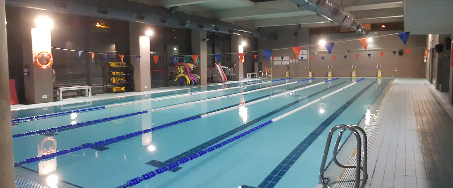 Panorámica lateral de la piscina de entrenamiento climatizada, con barandilla de acceso y diverso equipamiento de baño