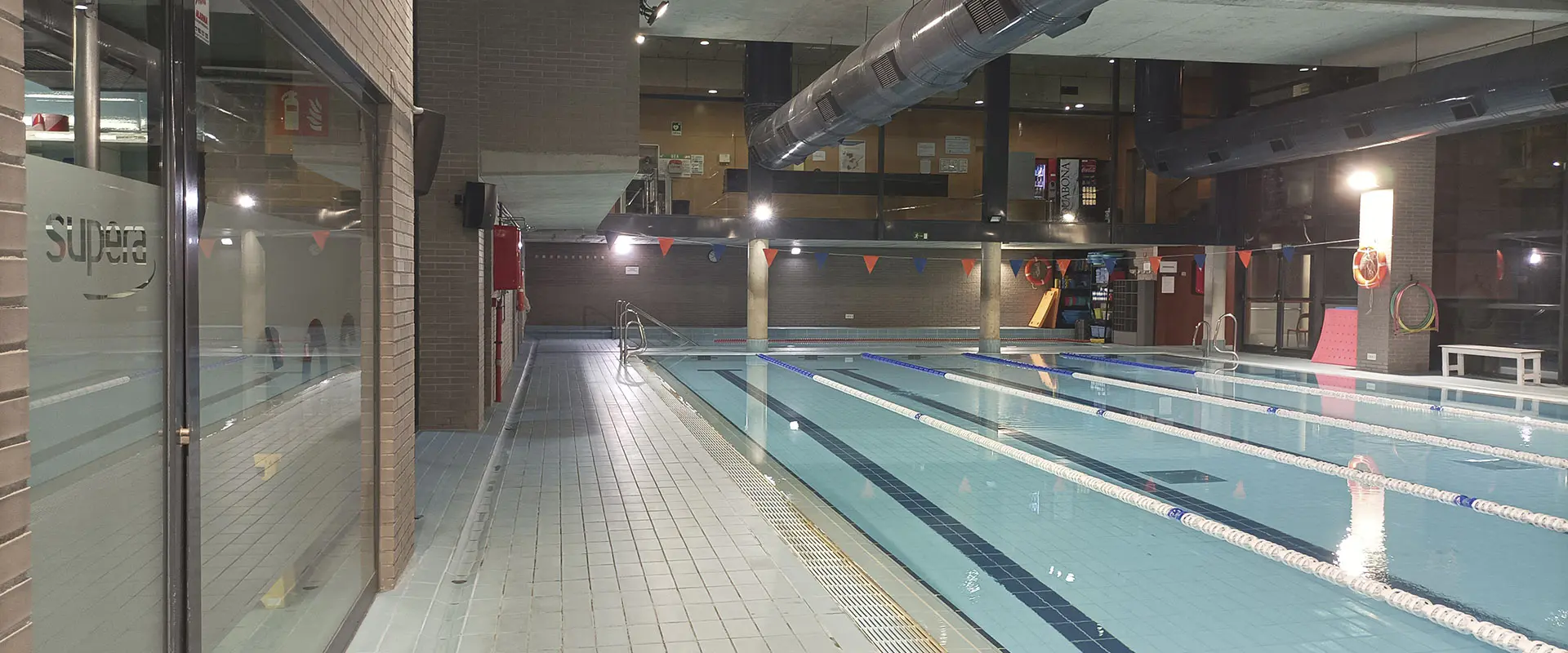 Vista lateral de la piscina de entrenamiento climatizada, con la sala de socorrismo en primer plano, a la izquierda
