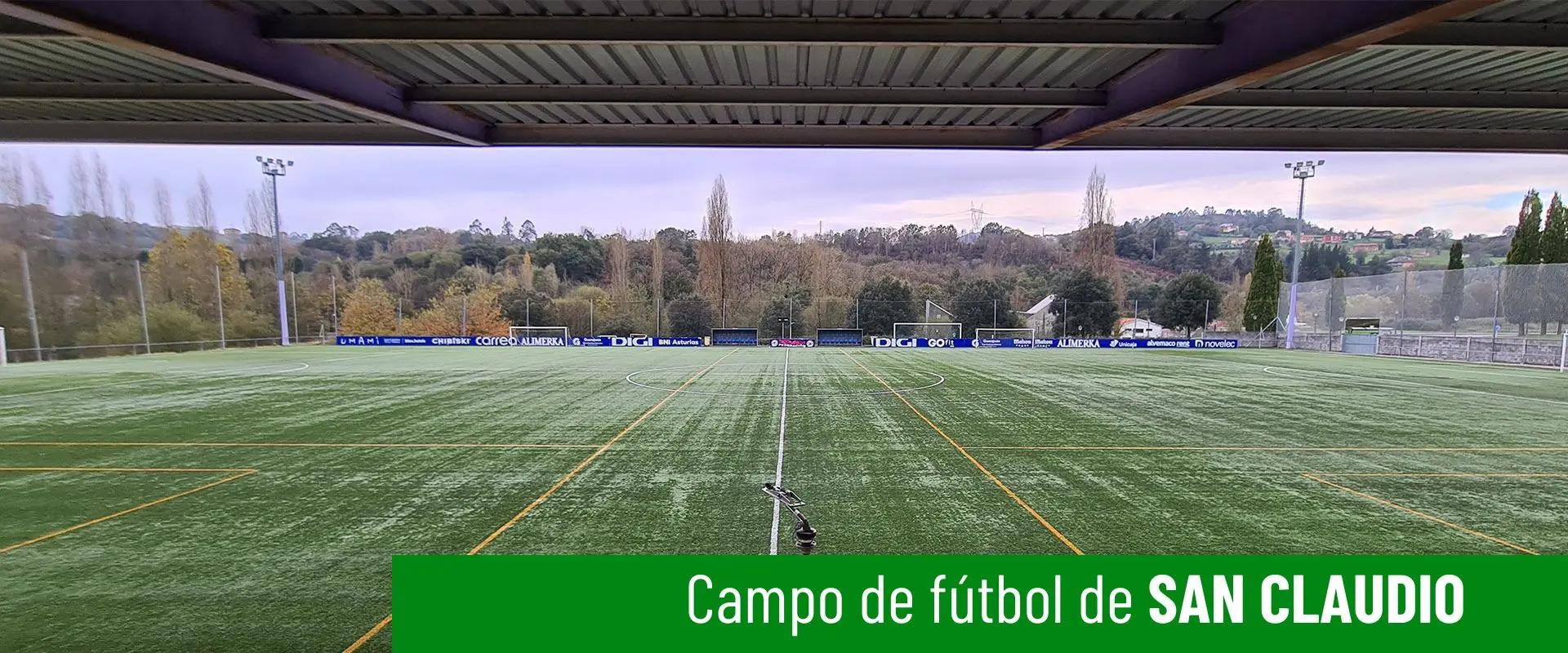 Imagen del campo de fútbol de San Claudio. Vallas publicitarias al fondo. Detalle de cubierta de las gradas en primer plano 