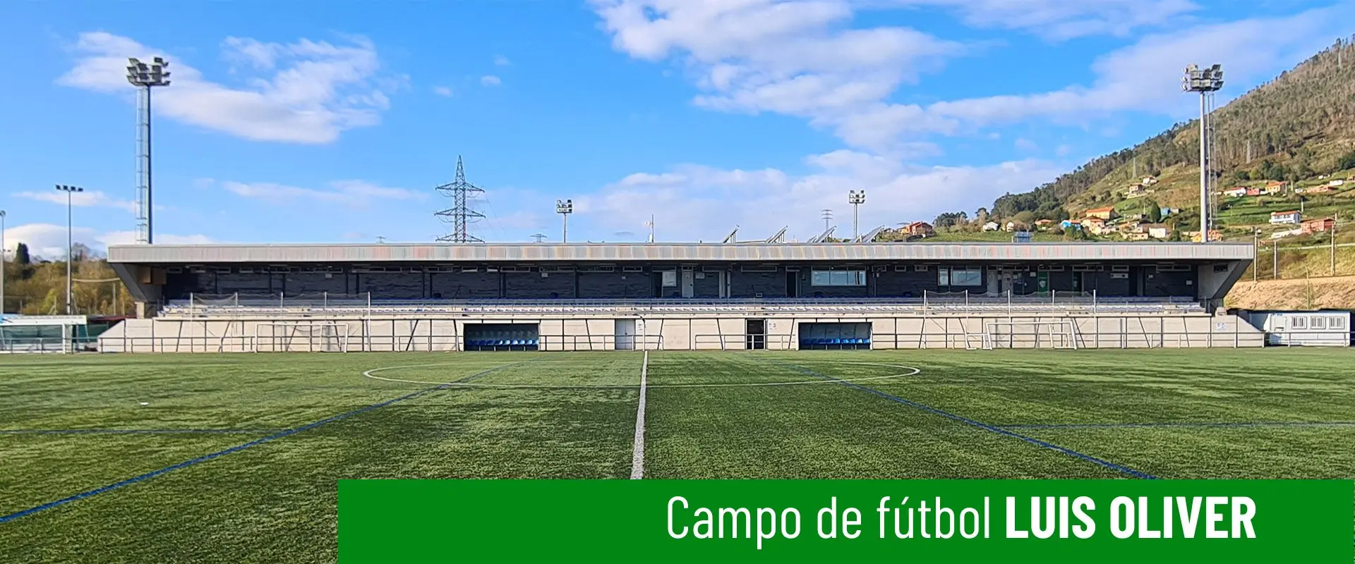 Imagen del campo de fútbol Luis Oliver. Terreno de juego a pie de campo. Línea blanca divisoria central. Gradas al fondo 