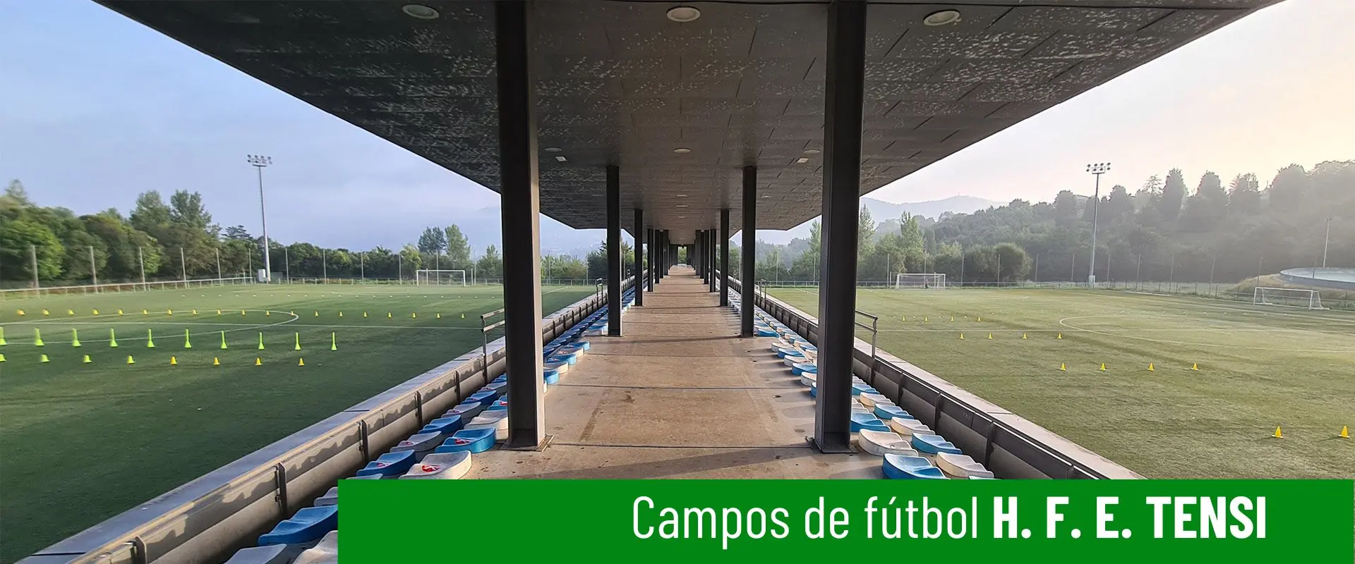 Campos de fútbol H. F. E. Tensi. Pasillo cubierto de acceso a gradas, con columnas. Dos campos de fútbol 11 a los lados 