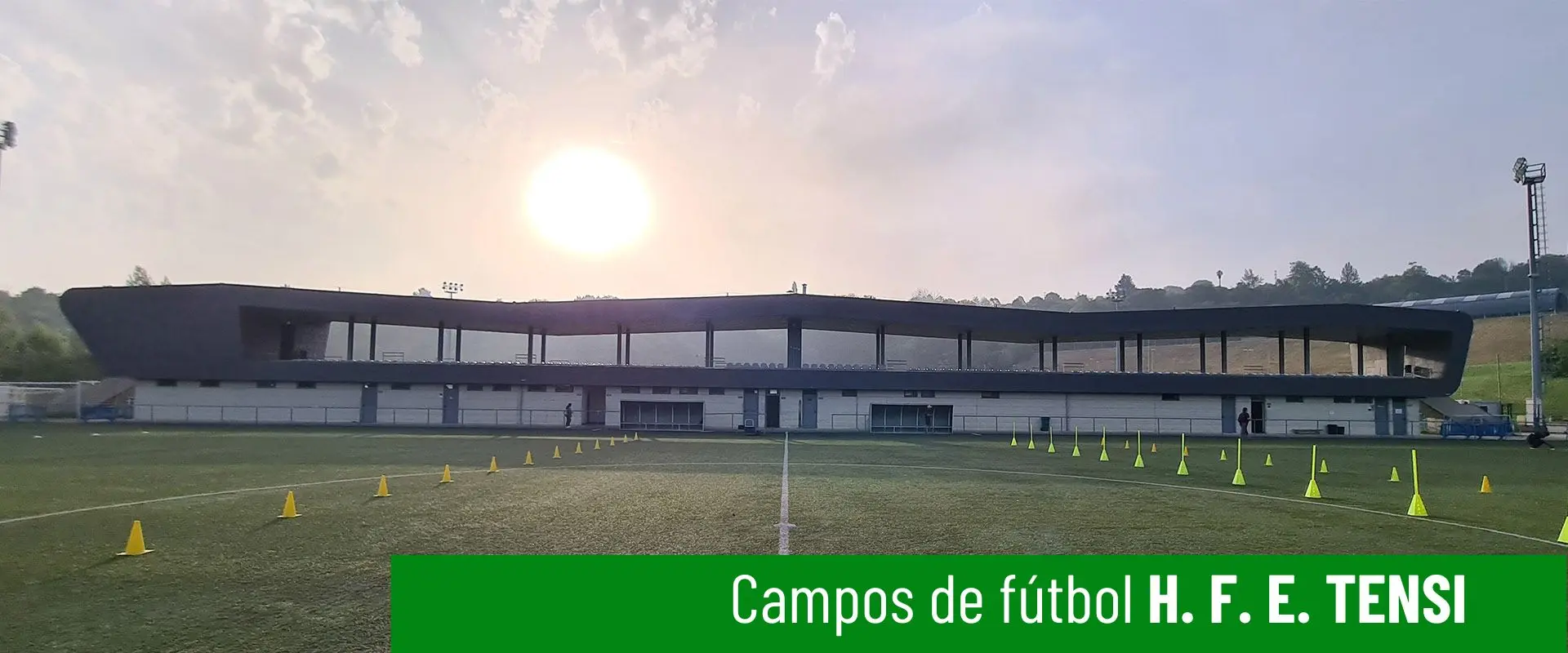 Campos de fútbol H. F. E. Tensi. Terreno de juego a pie de campo. Línea blanca divisoria central. Gradas al fondo 