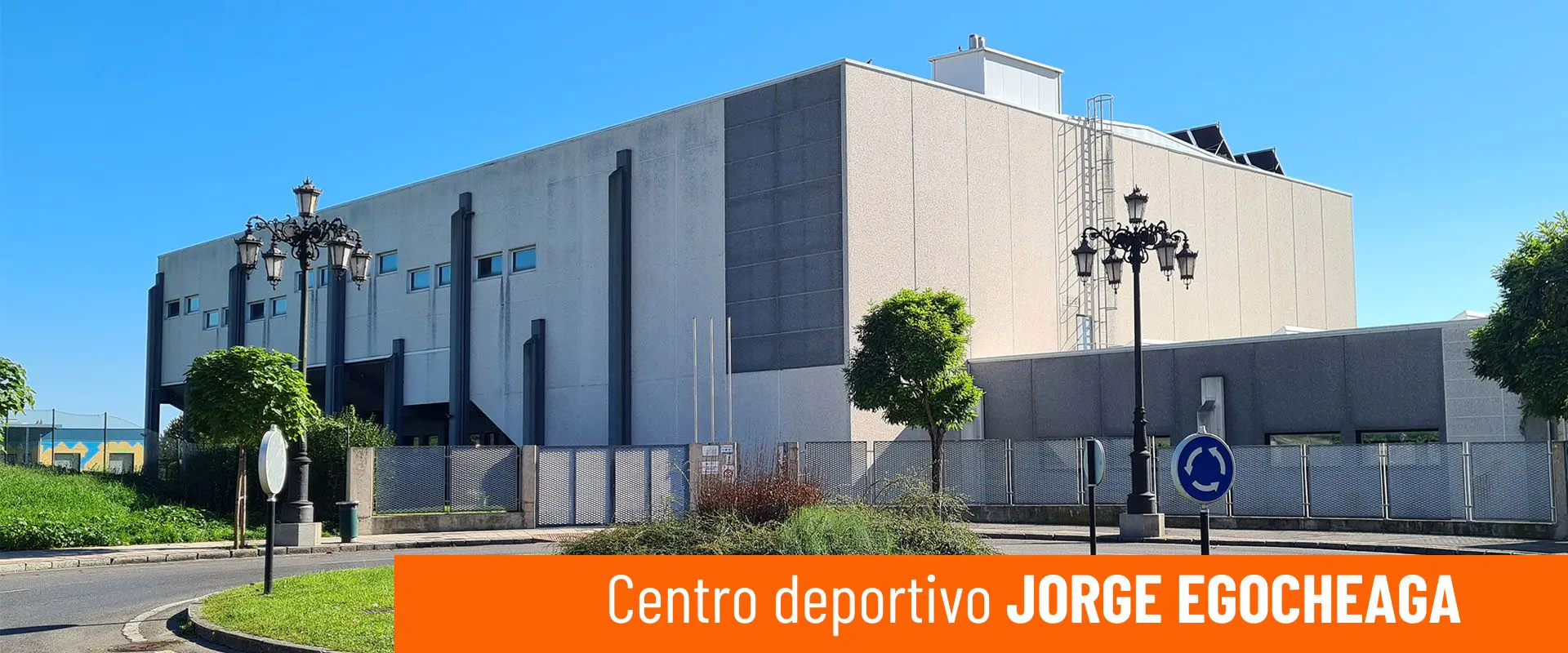 Vista exterior del Centro Deportivo Jorge Egocheaga, con vallas perimetrales y rotonda exterior ajardinada 