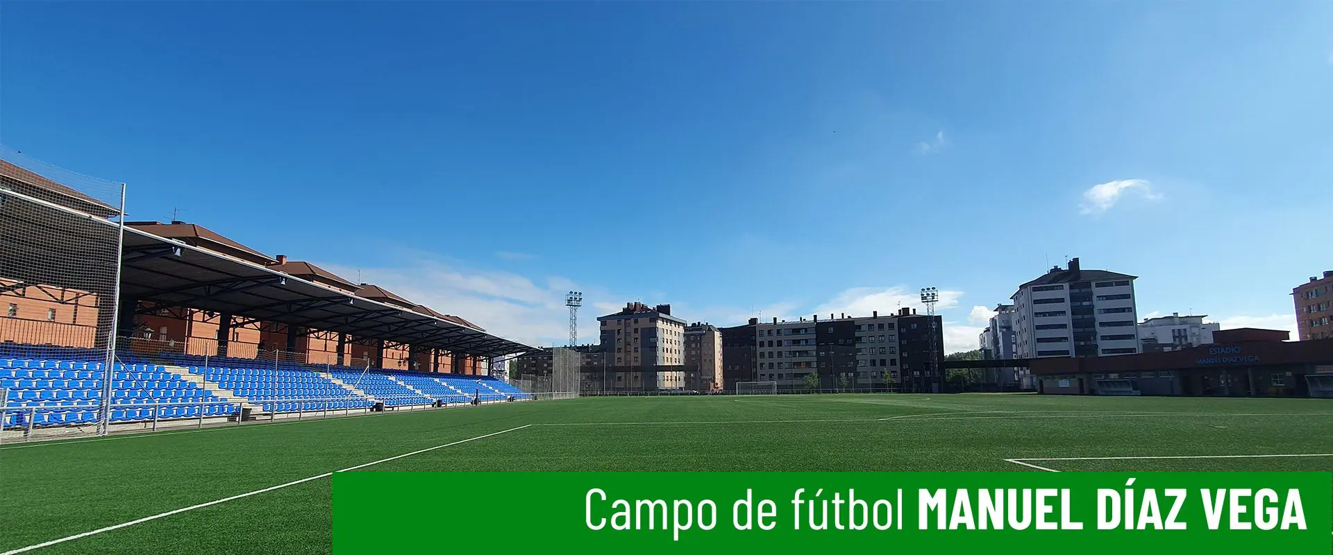 Estadio de fútbol Manuel Díaz Vega. Vista frontal parcial del campo. Gradas al lado izquierdo y edificios al fondo 