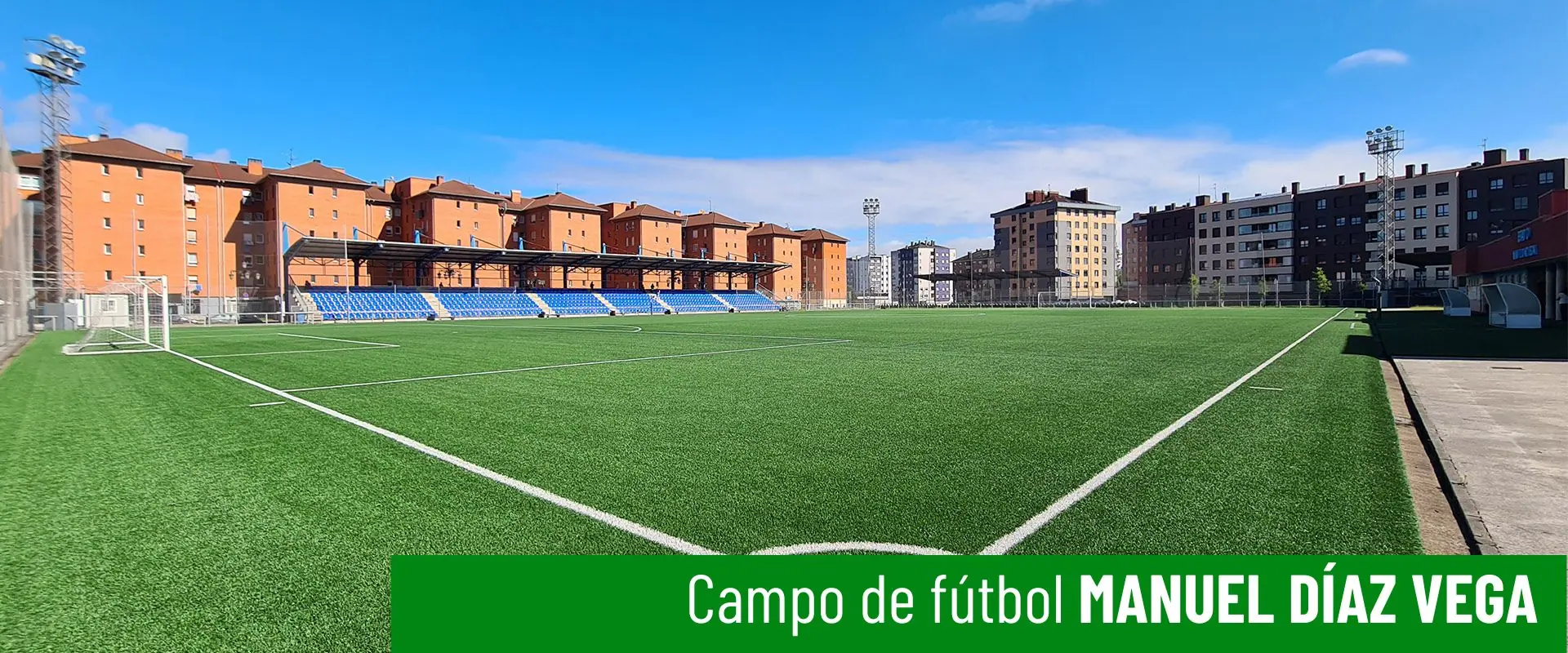 Estadio de fútbol Manuel Díaz Vega. Terreno de juego a pie de campo desde un córner. Grada en un lateral y edificios al fondo 
