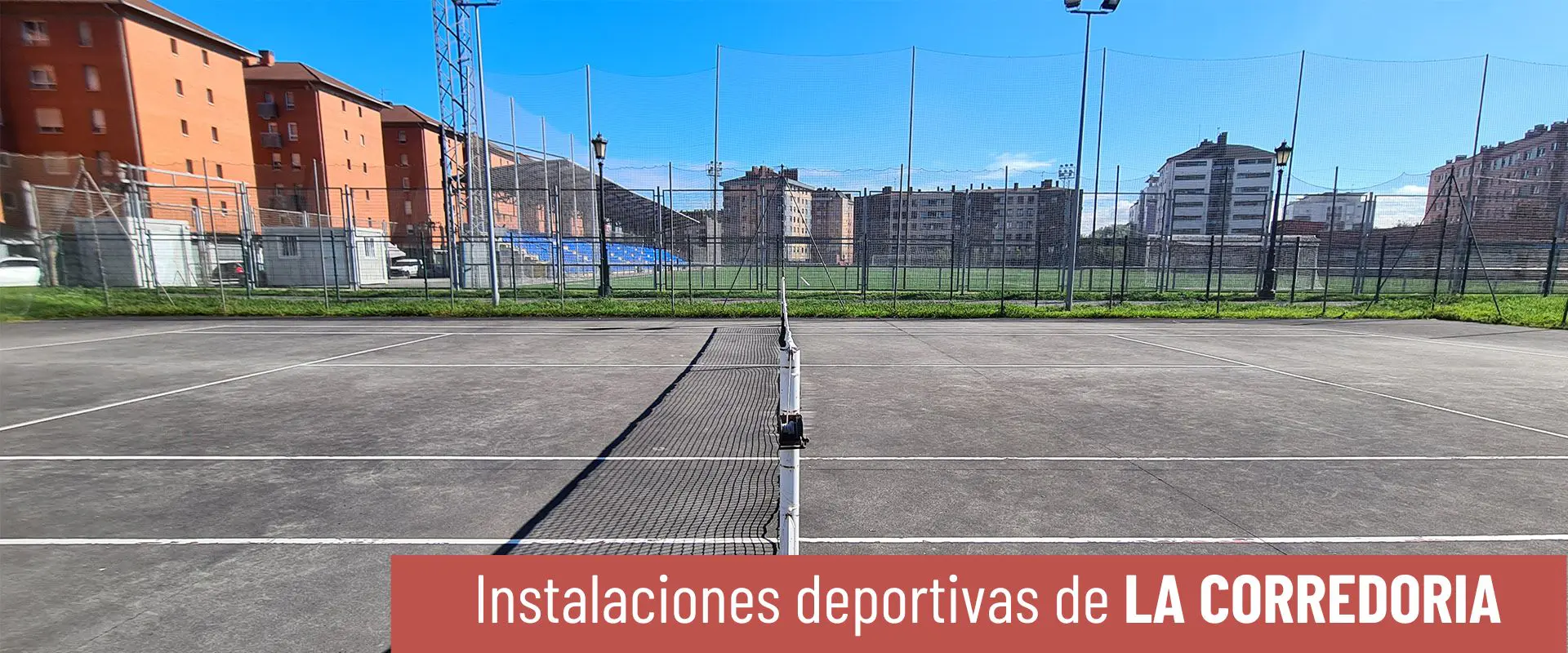 Pistas de tenis y hockey La Corredoria. Foto lateral de pista de tenis, con la red en el centro. Estadio Díaz Vega al fondo 