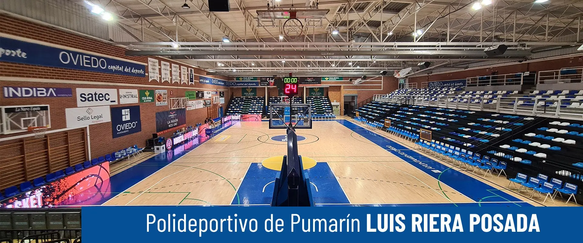 Polideportivo de Pumarín Luis Riera Posada. Foto frontal de pista polideportiva desde la grada. Canastas, marcador y gradas 