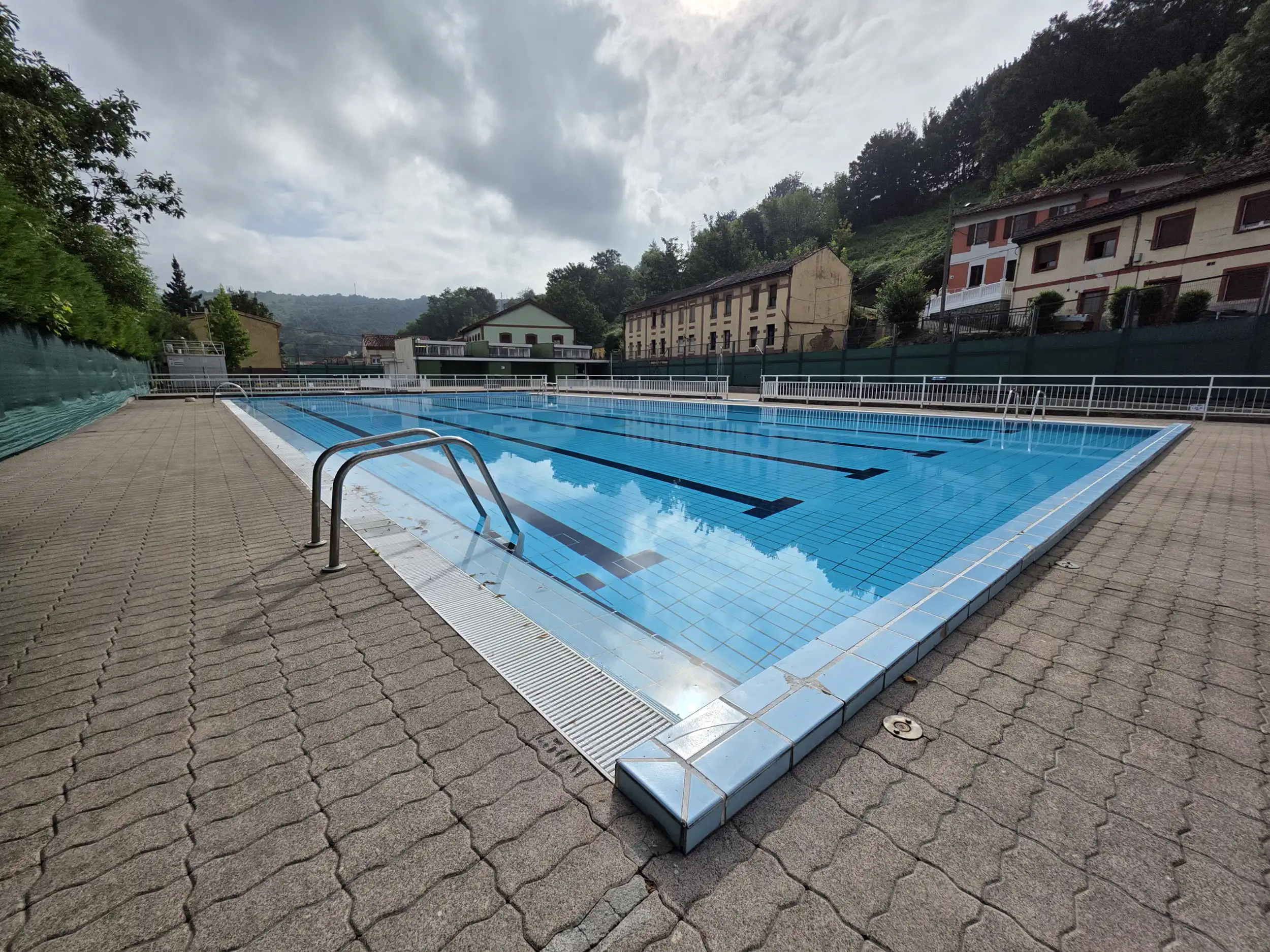 Vista de la piscina desde una esquina con la escalerilla de acceso al agua en primer plano