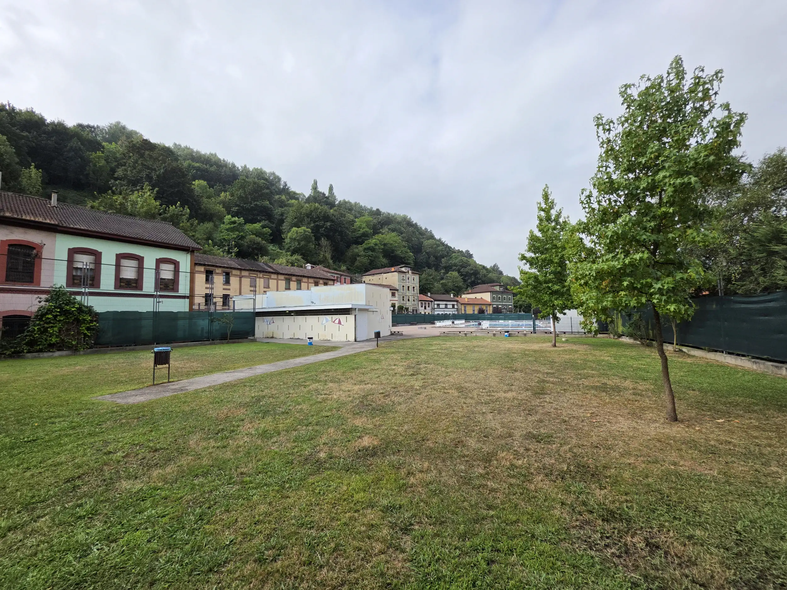 vista de la zona de playa con árboles, edificio de servicios y piscinas al fondo
