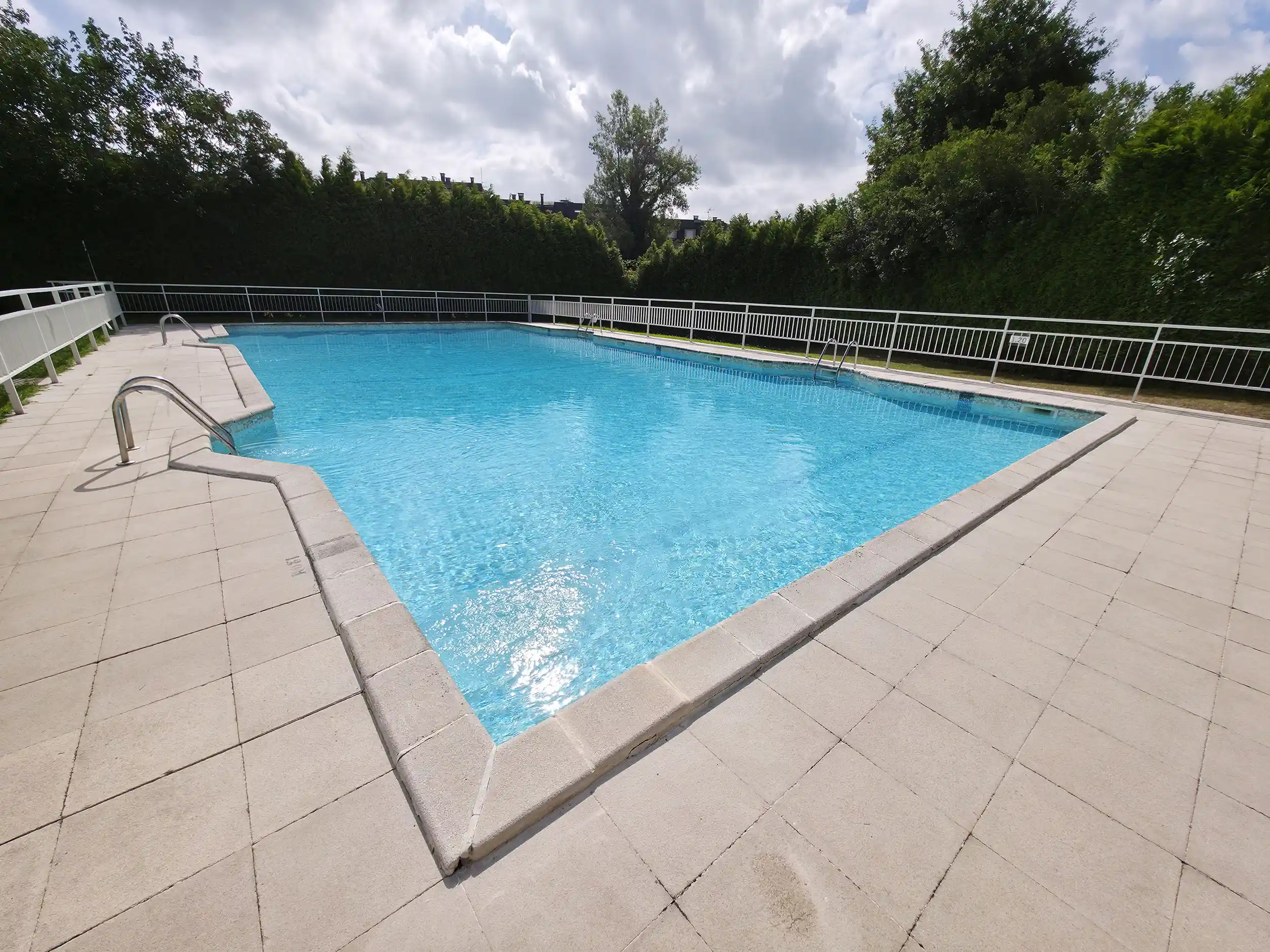 Vista de la piscina desde una esquina con la escalerilla de acceso al agua a la izquierda