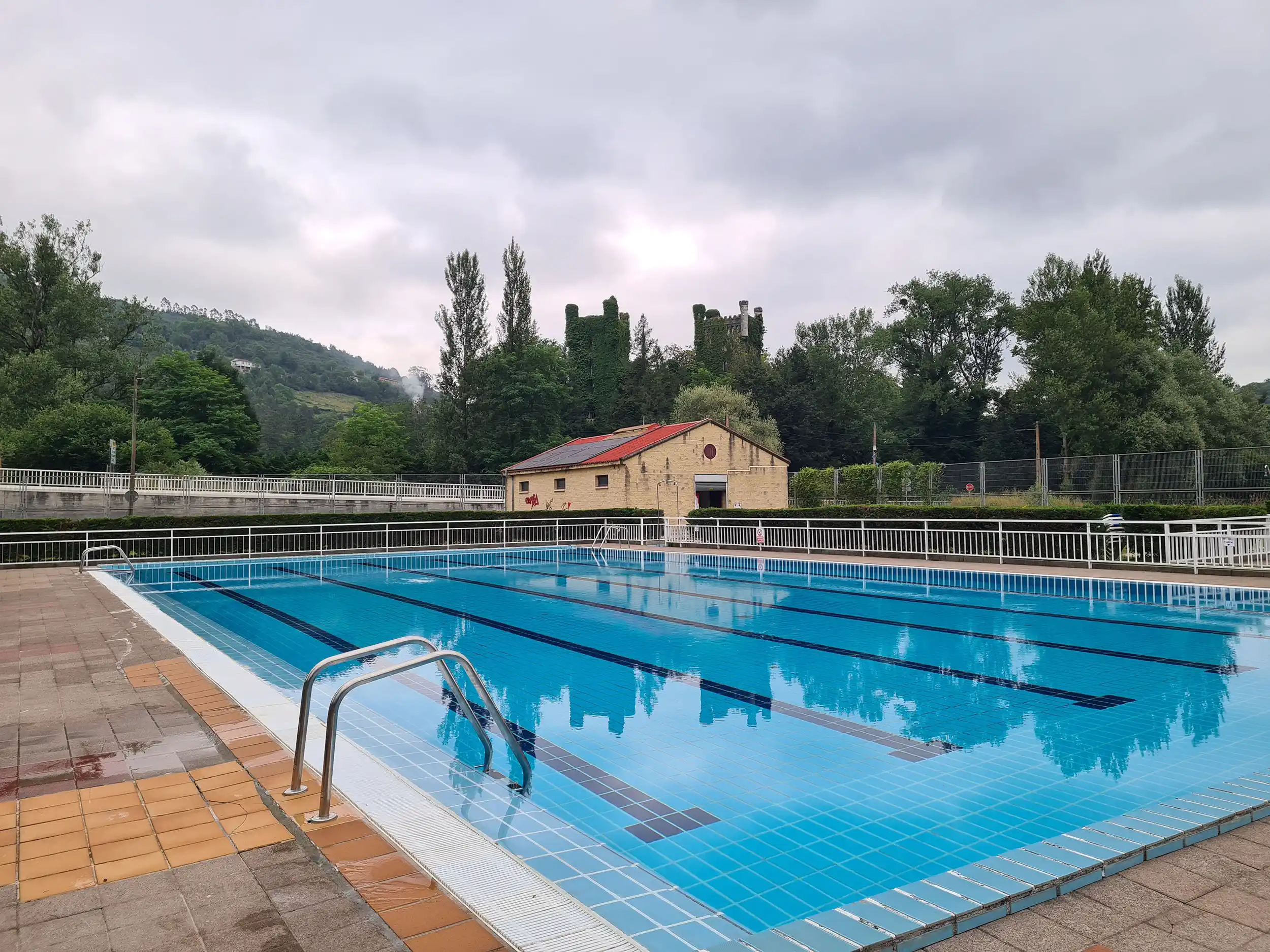 vista de la piscina con el edificio de servicios y las torres del castillo de Las Caldas al fondo