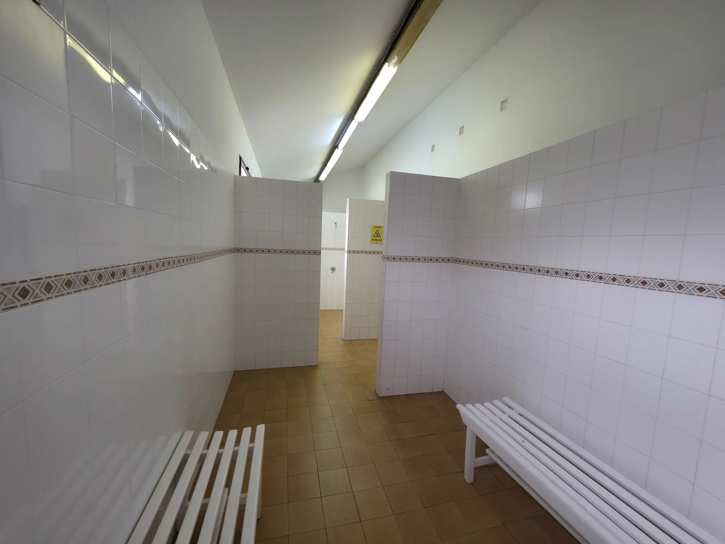 Zona de vestuario con bancos y primer plano y duchas al fondo