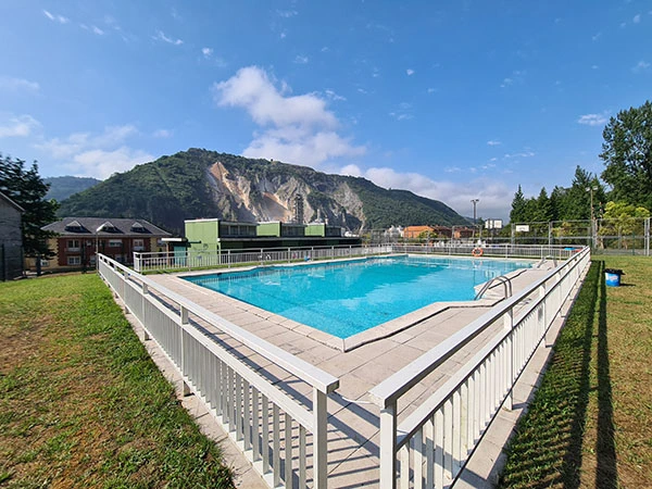Vista de la piscina, al fondo edificio de servicios y los tejados de algunas viviendas de Olloniego