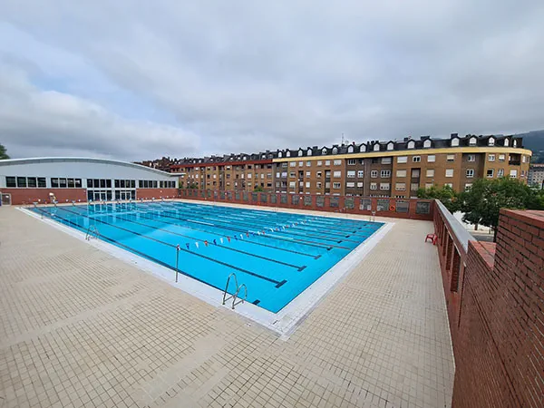 vista elevada de la piscina desde una esquina. A la izquierda el edificio de las piscinas cubiertas