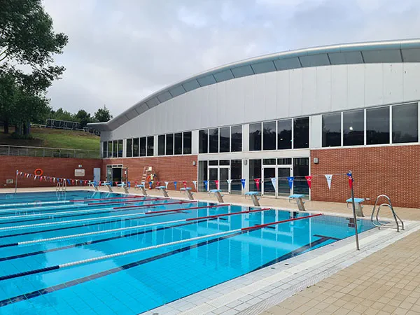 vista parcial de un fondo de la piscina con el edificio de piscinas cubiertas en primer plano