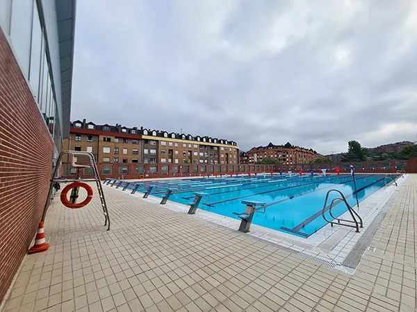 vista de la piscina desde una esquina con la silla de socorrista y la escalerilla de acceso al agua en primer plano