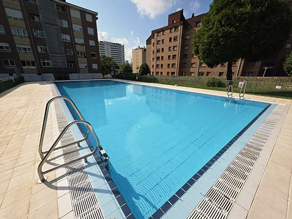 Vista de la piscina desde una esquina con edificios de viviendas al fondo